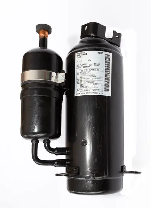 Schwarzer Daikin-Kompressor mit zwei angeschlossenen Rohren. Auf dem Gehäuse sind technische Informationen und Warnhinweise auf einem Aufkleber zu sehen.